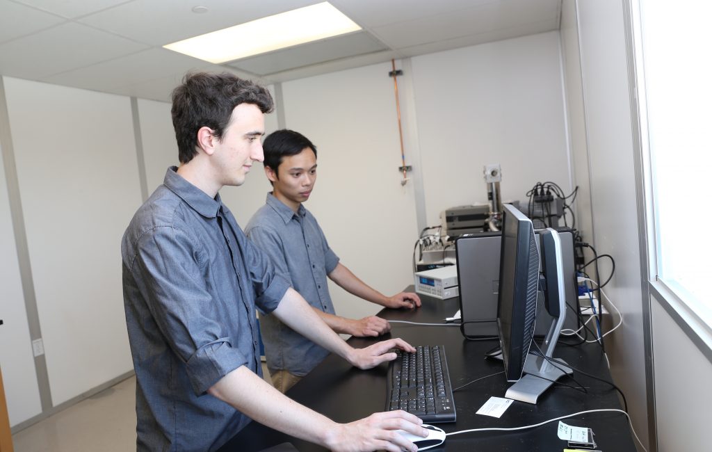 Two young men standing in front of a computer